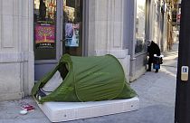 A woman stands in a street next to a homeless tent, in Paris, France, Tuesday, Dec. 21, 2021. 