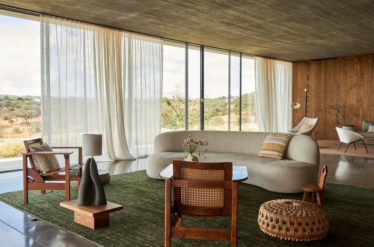 In the living room of the Le Labo co-founder Eddie Roschi’s country home in the Alentejo region of Portugal, a Pierre Augustin Rose sofa and vintage chairs share the space with cushions, a ceramic lamp and a wooden table all designed by Flores textile studio and a pouf woven from bunho (a grasslike marsh plant) from one of the few artisans in the country who still works with the material.