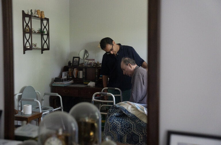 Robert Ingenito helping his father, Jerry Ingenito, get out of bed at their home in Mamaroneck, N.Y.