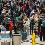 A crowd of travelers, many wearing backpacks and carrying bags, standing in a meandering line at an airport.