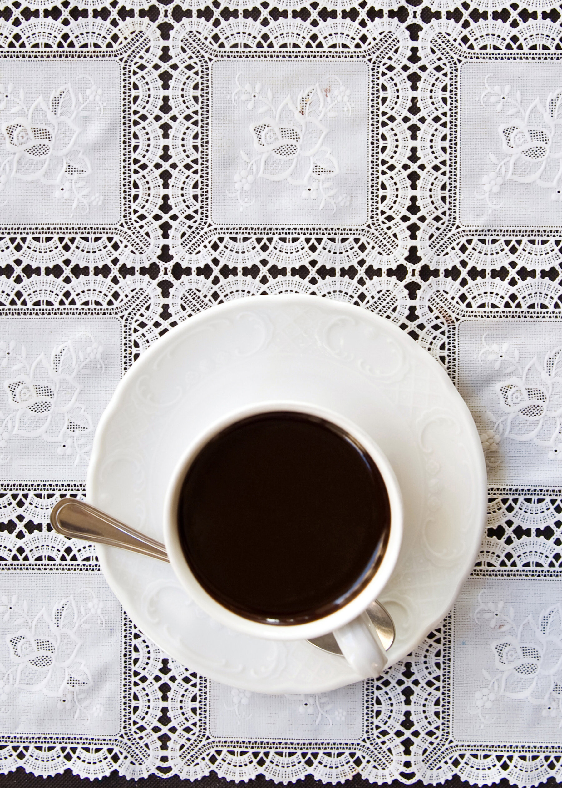 A cup of a thick, dark hot chocolate on a table that is covered with a white lace tablecloth. 