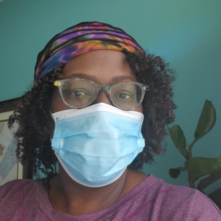 A woman wearing a surgical mask, a purple shirt and eyeglasses.