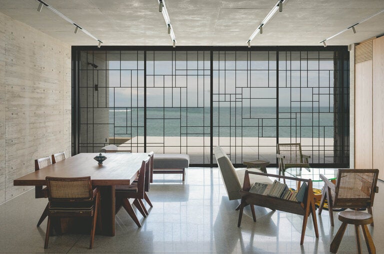 The open-concept living room at the artistic director Nigo’s seaside home in Japan frames a view of the Pacific Ocean and features dining and lounge chairs by Pierre Jeanneret and a coffee table by Isamu Noguchi.