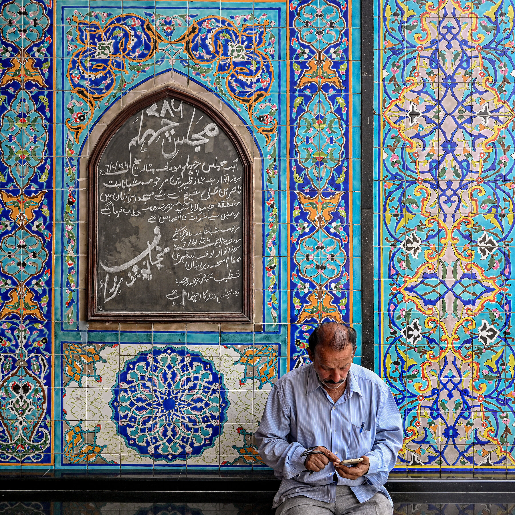 A person wearing a collared shirt rests against a wall that features vibrant blue tiling in geometric patterns. 