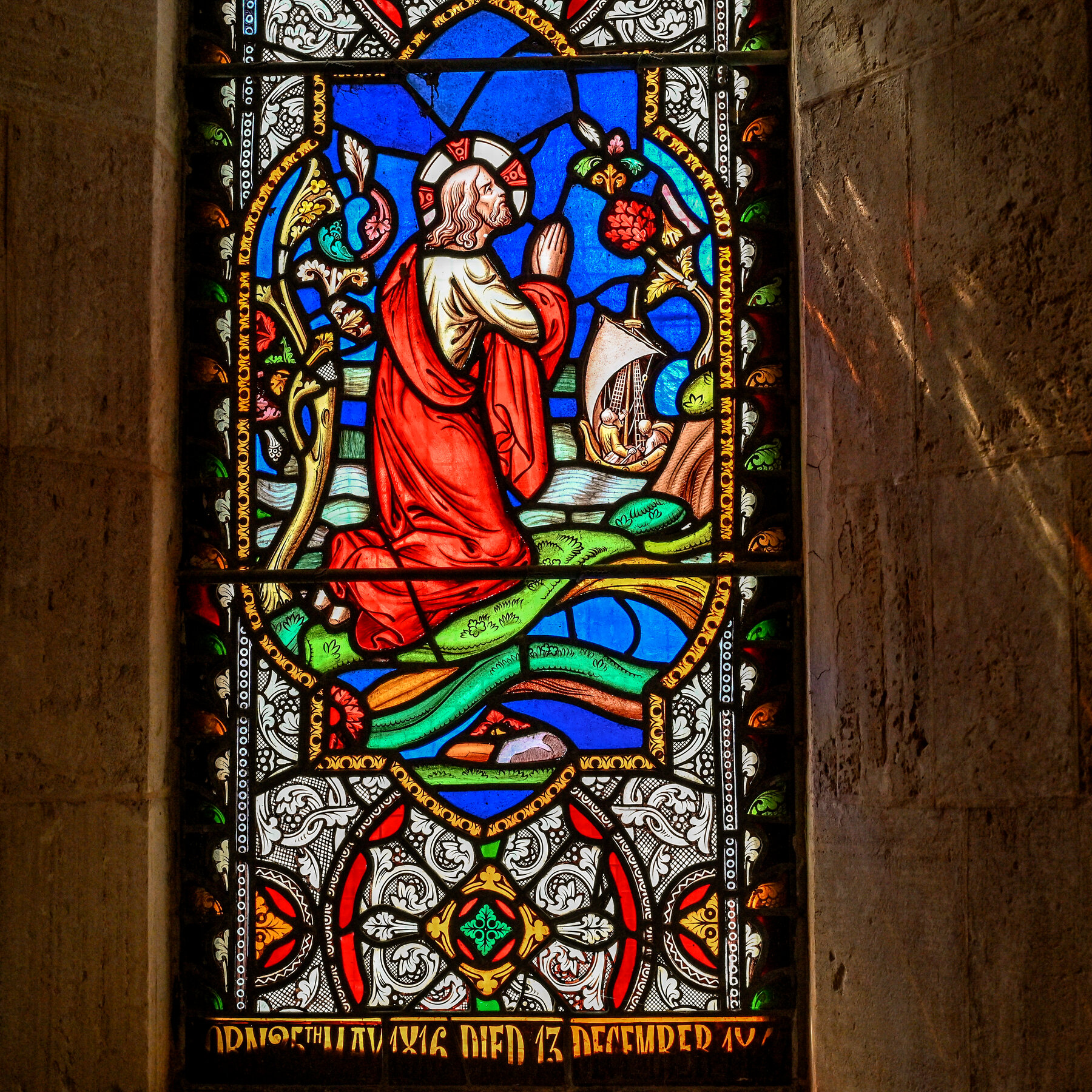 A close-up of a stained glass window depicting a man in a red robe kneeling in prayer. 