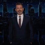 Jimmy Kimmel stands on a dimly lit stage, smiling.