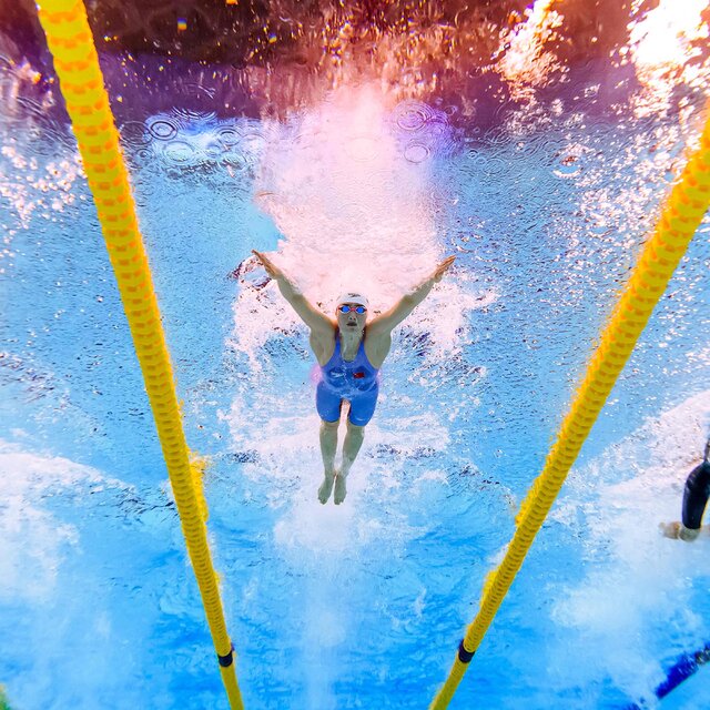 Three swimmers are seen racing in different lanes from an underwater view.