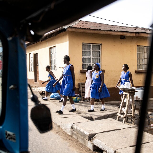 A view from inside a motor rickshaw of several schoolgirls in blue uniforms walking to school.