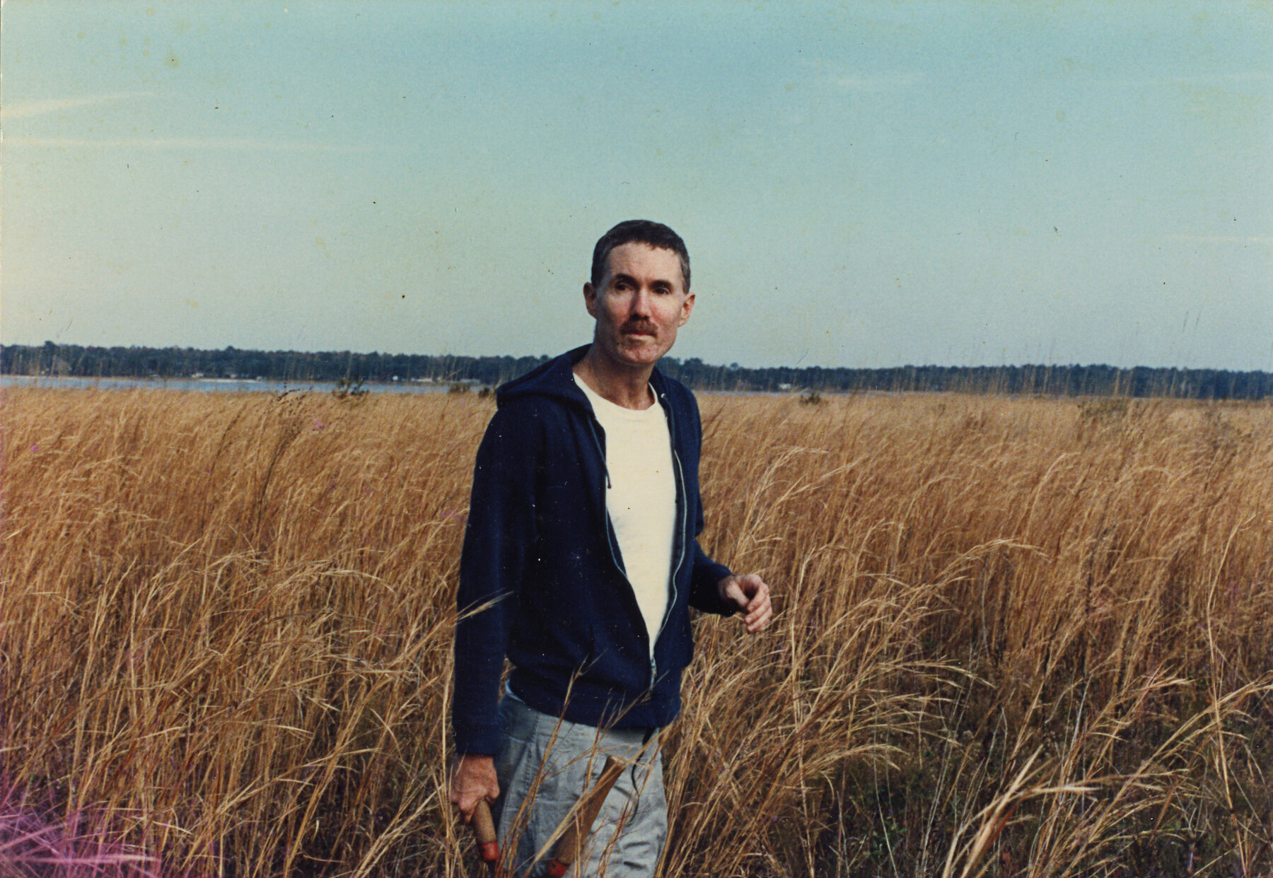 A man with a mustache and short brown hair stands amid brown reeds.