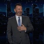 Jimmy Kimmel, in a gray suit, holds a hand on his chest and laughs.