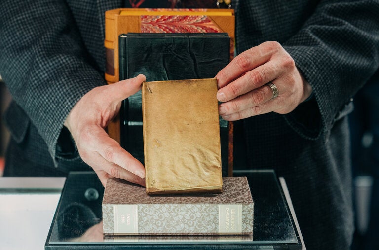 A small 17th-century book bound in human skin, held in front of a volume bound in leather. Roughly 50 reputed or confirmed skin-bound books are known to exist in libraries or private collections around the world. 