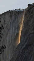 A photo of Firefall at Yosemite, showing a glowing yellow waterfall cascading down a sheer, massive rock face at dusk.