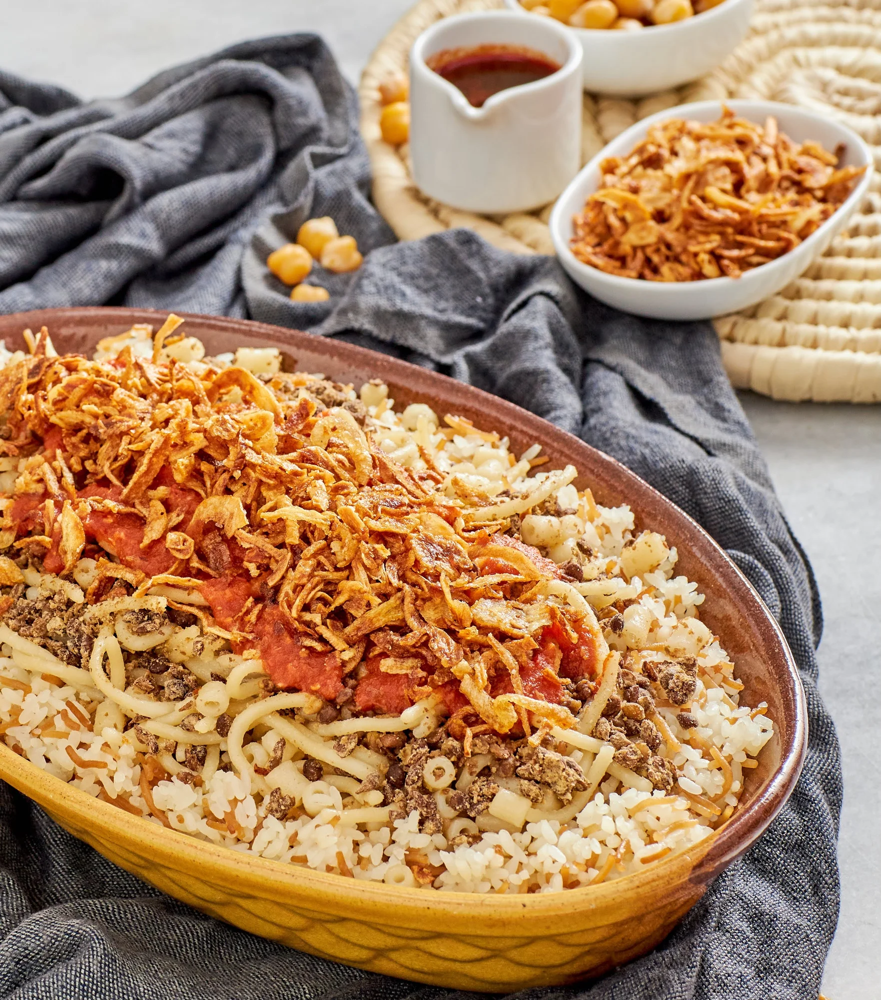 Savory Egyptian dish with pasta, lentils, rice, and crispy onions in a tomato sauce.