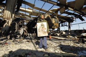 A Libyan holds a poster of Libya's leader Muammar Gaddafi at a naval military facility damaged by coalition air strikes last night in eastern Tripoli March 22, 2011. Pictures taken on a guided government tour.  REUTERS/Zohra Bensemra