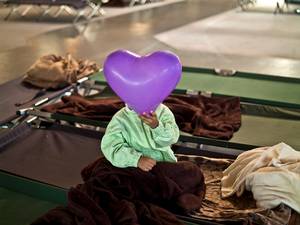 22 September 2015: An Afghan refugee child covers his face with a balloon while he and other migrants spent the night in a shelter near Graz, Austria