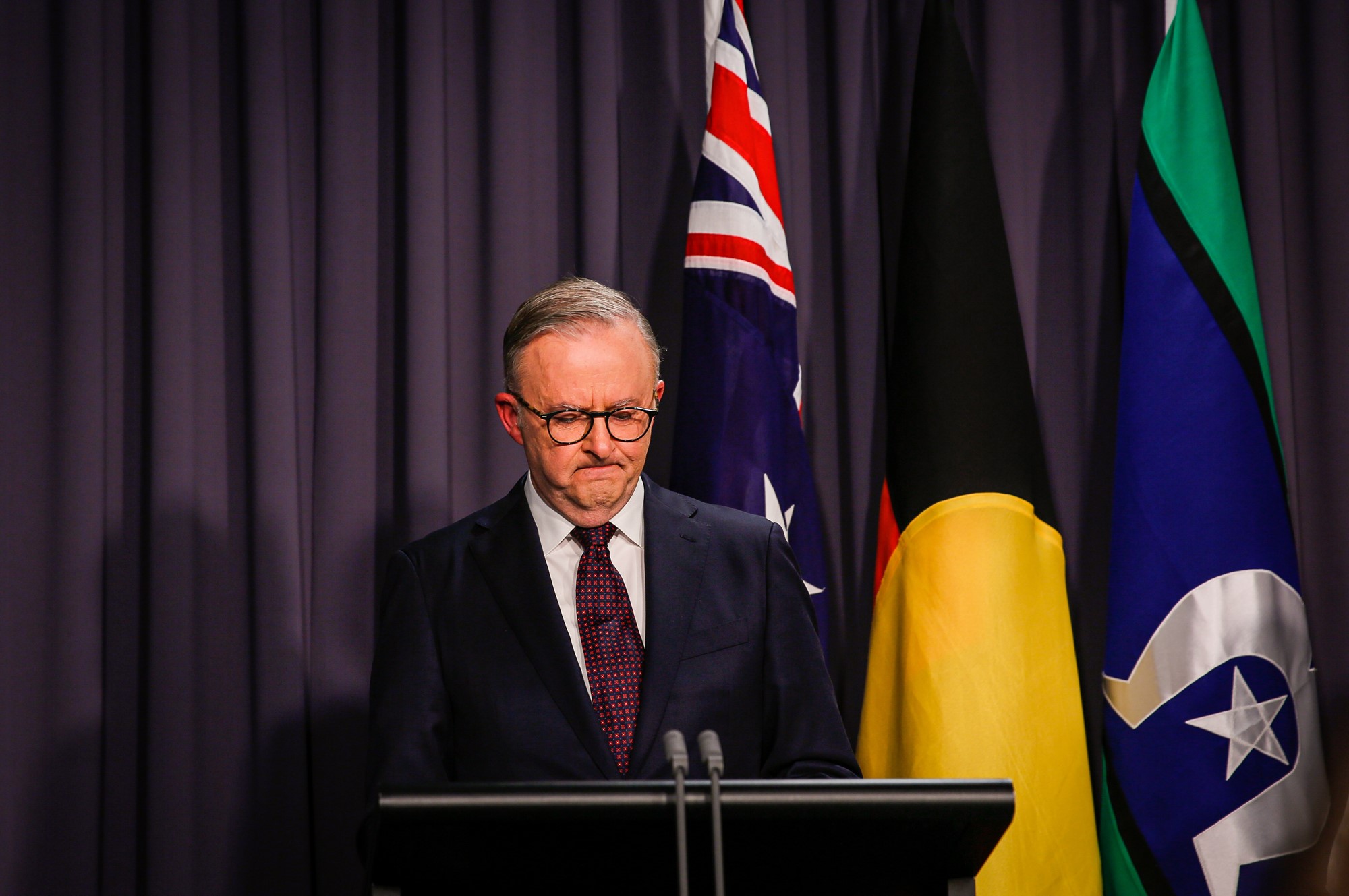 Anthony Albanese wearing a suit looks down while standing behind a lecturn.