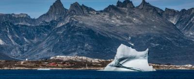 An iceberg floating in the ocean with mountains in the background.