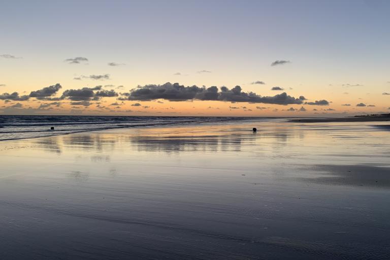 Twilight at a serene beach with reflections on wet sand and wispy clouds above.