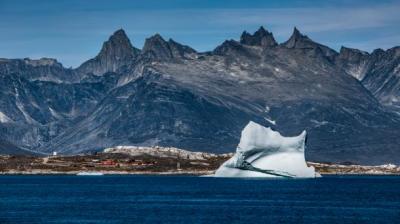 An iceberg floating in the ocean with mountains in the background.