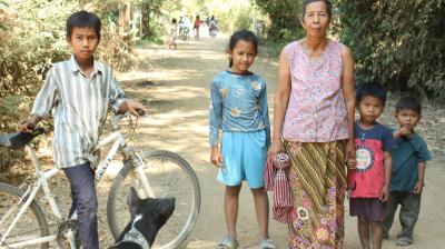 A group of people standing next to a bicycle on a dirt road.