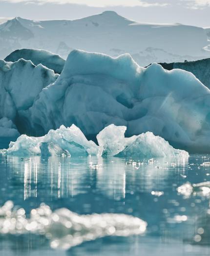 Glacial icebergs floating in a calm, icy water with a hazy mountain backdrop.