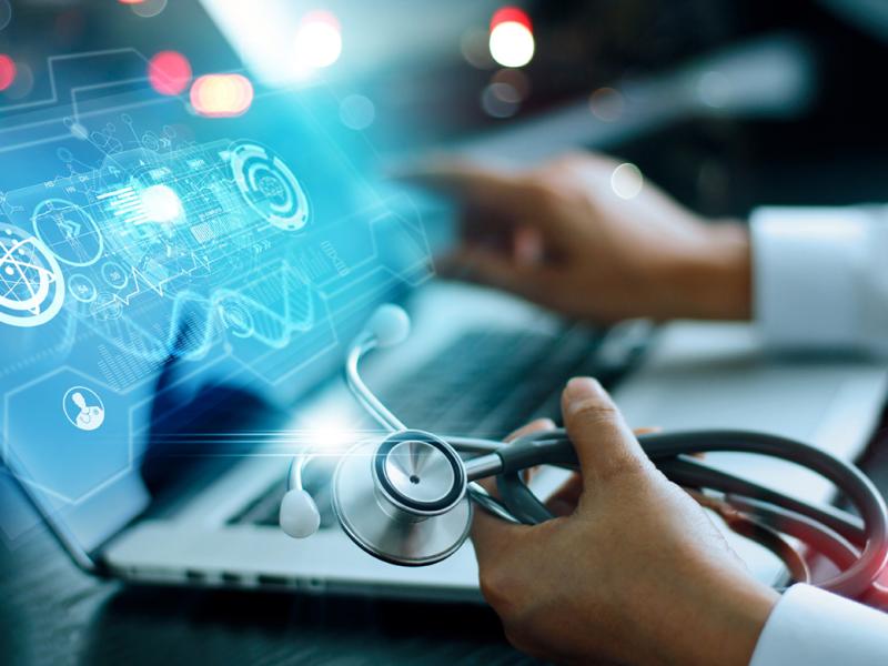 Physician hand with stethoscope, looking a futuristic image on laptop