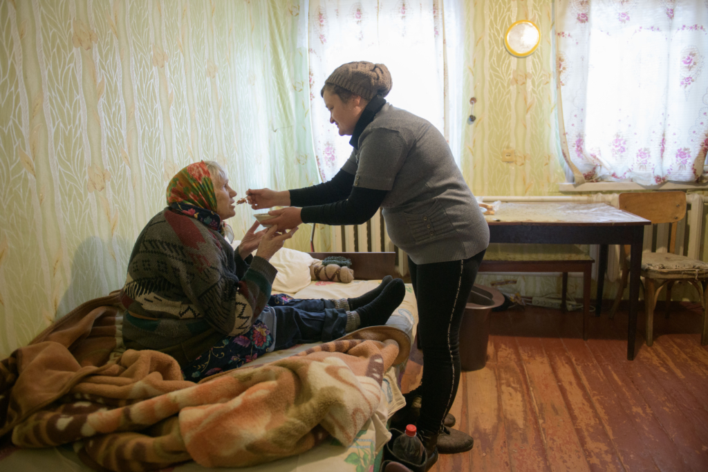 Care worker feeding older woman say on a bed.
