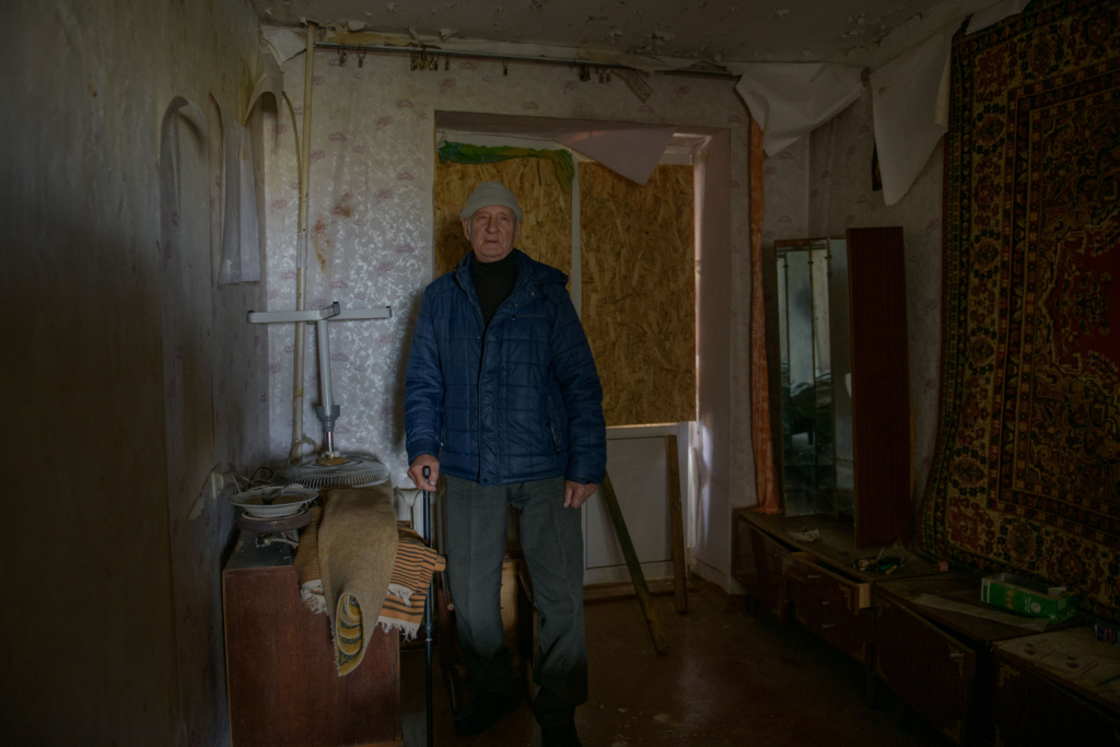 Older man with walking stick stood in flat that needs repairs.