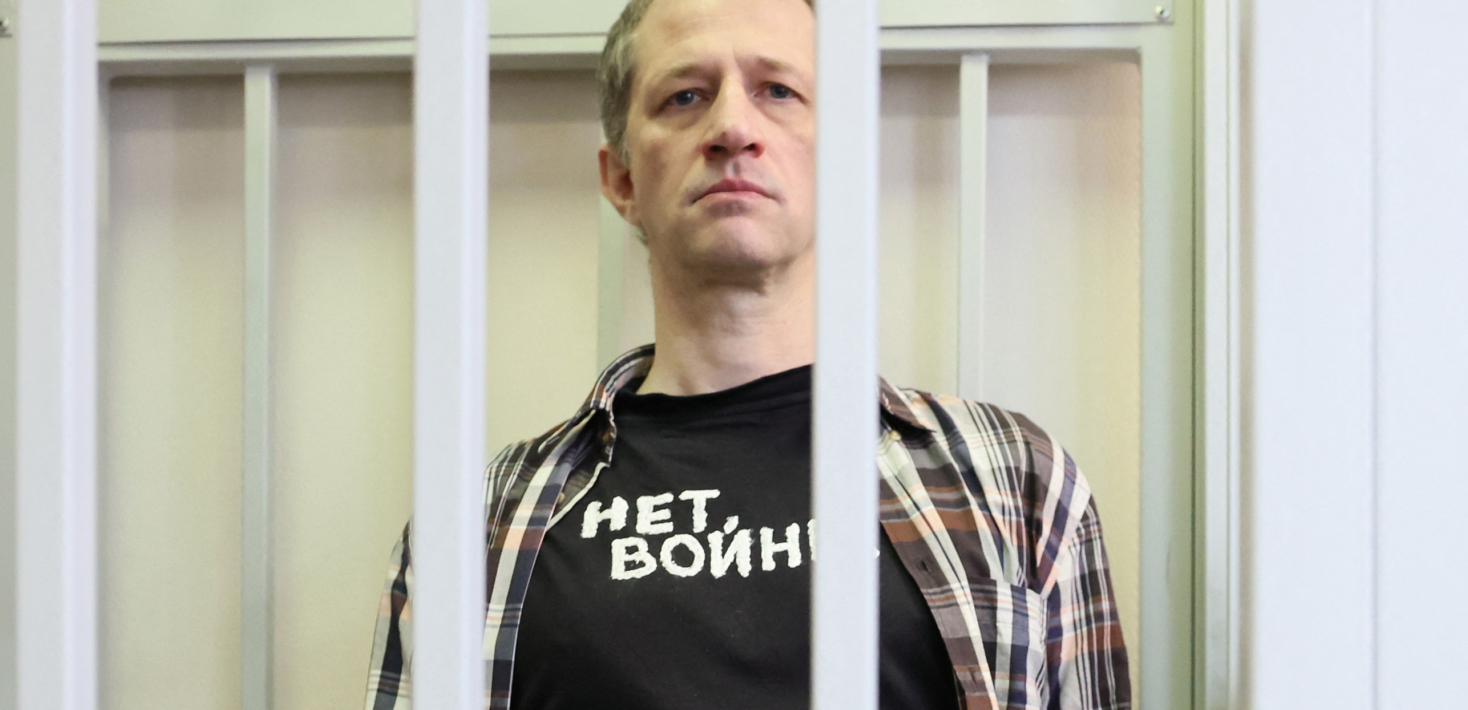 Russian journalist Roman Ivanov wearing T-shirt reading as "No war" stands inside a defendants' cage handcuffed after being sentenced to seven years in prison for criticising the Ukrainian offensive in social media posts, in Korolyov, Moscow region, on March 6, 2024