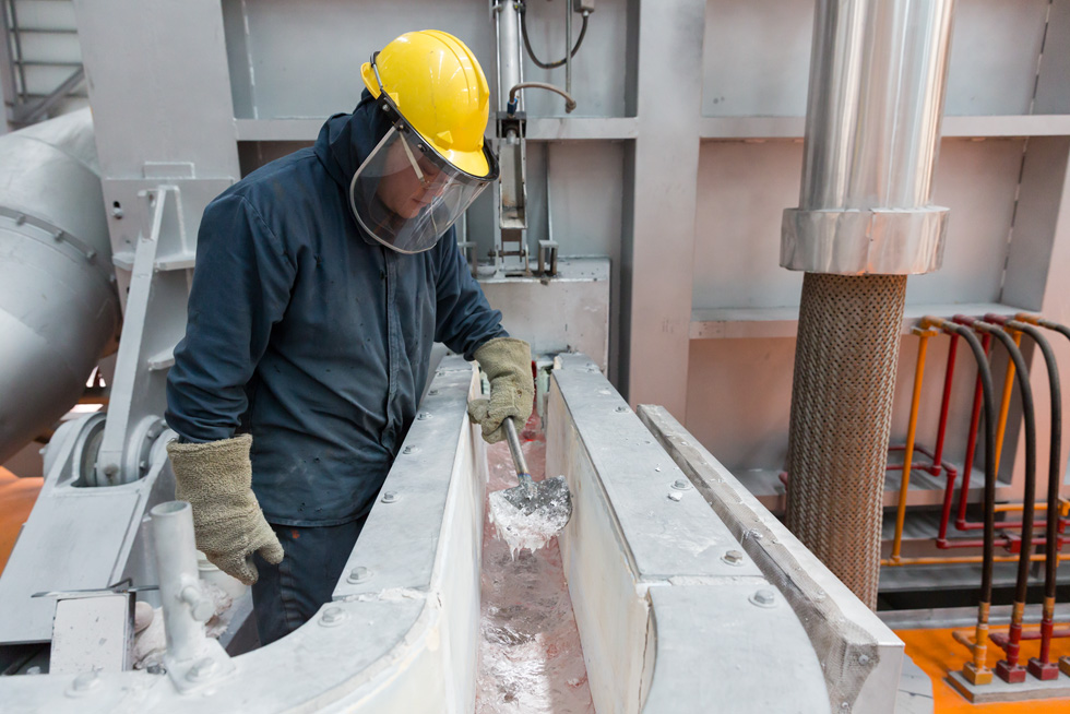 A factory worker monitors the smelting process at an aluminum production plant.