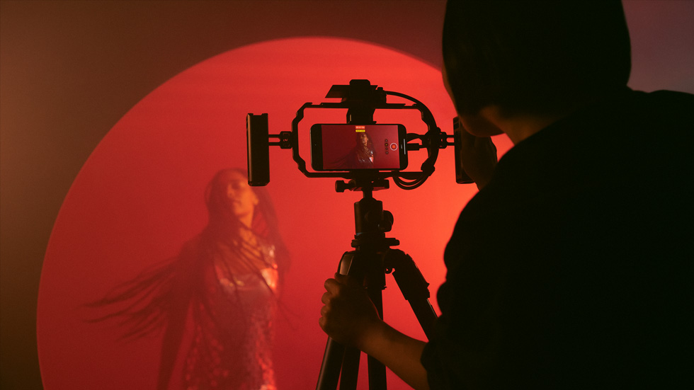 Nuotrauka asmens, naudojančio „iPhone“ ant trikojo spalvotam moters vaizdo įrašui filmuoti