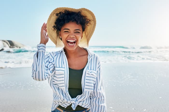 Foto de una mujer en la playa. Lleva una camisa de manga larga y un sombrero de ala ancha.