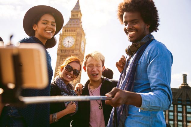 Group of four friends taking a selfie with a selfie stick while traveling overseas