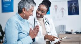 Image of a woman in a blue sweater smiling while speaking with a female healthcare provider in a white lab coat with a stethoscope