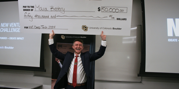 Grinning man stands with a giant check for $50,000 held over his head