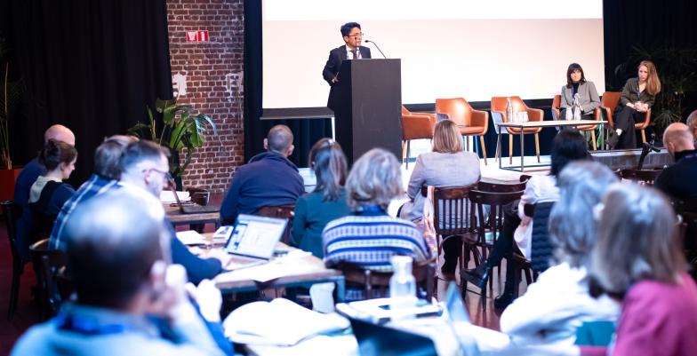 Picture from the event: speaker in the podium, two other speakers sitting beside him and the audience