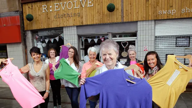 A group of women are smiling holding up clothes in front of the R:evolve store.