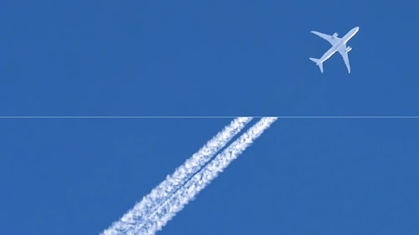 Airplane against blue sky with contrails trailing behind
