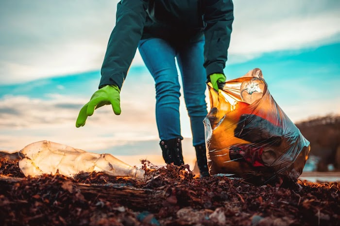 A person wearing gloves picking up trash and placing it in a garbage bag