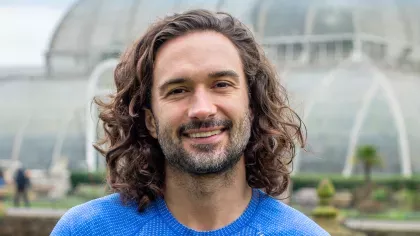 A man with long dark hair, Joe Wicks, stood in front of Kews palm House a large glass building.