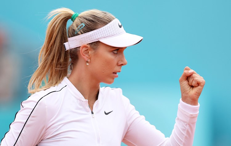 Katie Boulter, wearing a white Nike fleece and hat, clenching her fist in celebration on court at the Madrid Open
