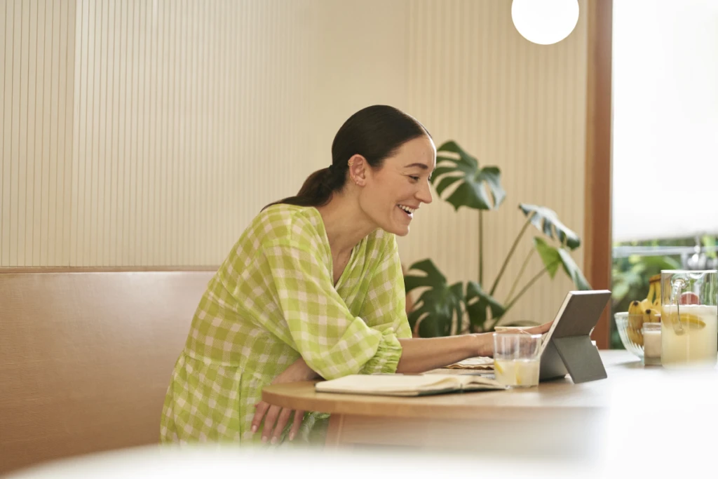 Woman sitting in kitchen working on 2-in-1 tabletin laptop mode.