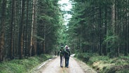 Ein Pärchen von hinten, wie es Arm in Arm durch einen Wald spaziert. © tilla eulenspiegel / photocase.de Foto: tilla eulenspiegel / photocase.de