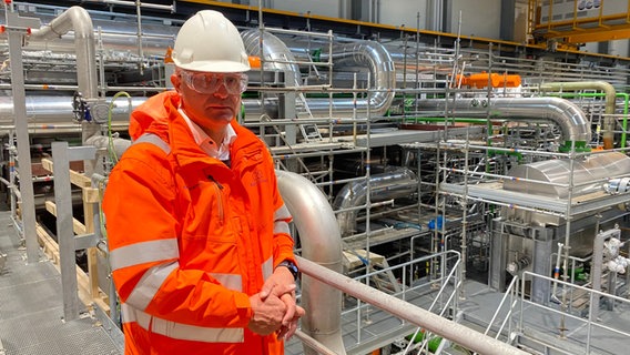 Der Bürgermeister von Esbjerg, Jesper Frost Rasmussen, steht mit Sicherheitshelm in einer Halle der Meerwasser-Wärmepumpe. © NDR Info Foto: Anna Marohn