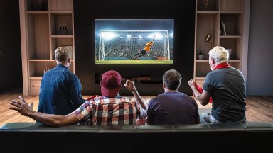 Four men sitting on sofa and enjoying football match on TV
