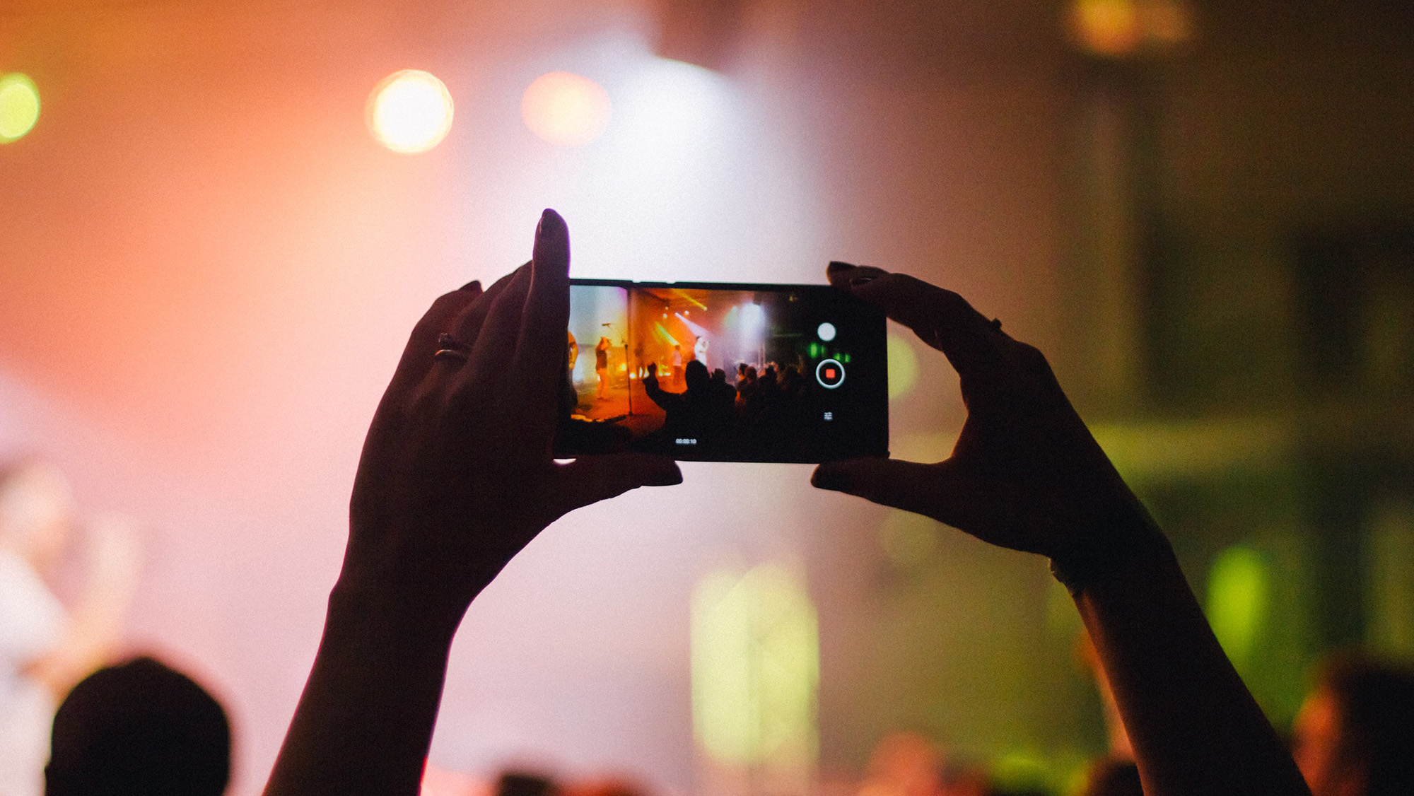 Two hands reaching out from a crowd with a phone to record someone on stage.