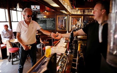 A customer pays for his drink with cash at the bar of a pub in central London on 19 July 2021