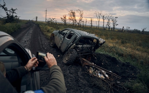 A Ukrainian soldier takes a photo of a burnt-out vehicle on the road