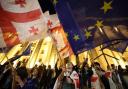 TOPSHOT - Protesters wave Georgian national and European flags during a demonstration outside the parliament building as they protest against a draft bill on 