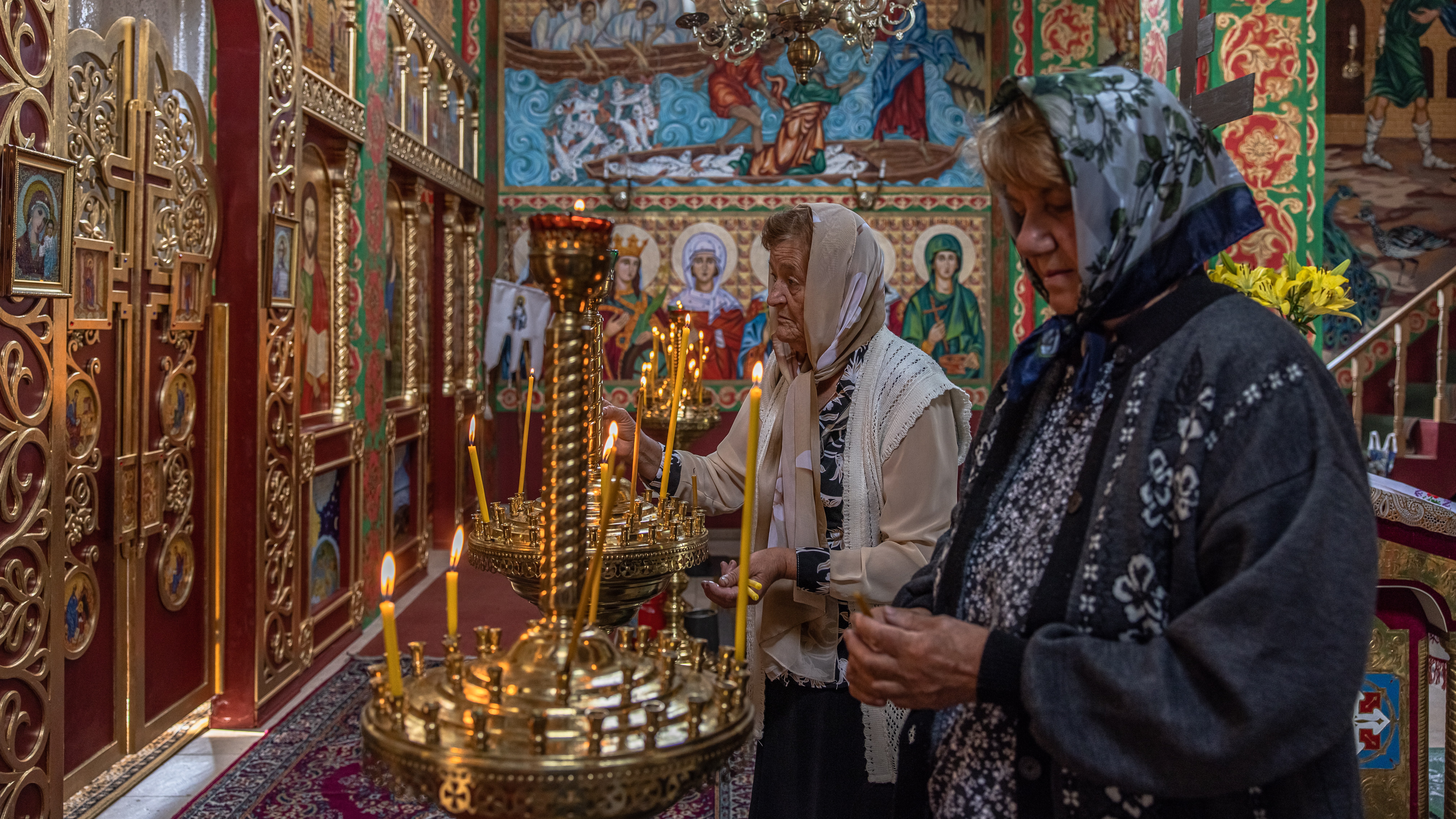 Women light candles before morning service at a church in Moshchun, Kyiv Oblast
